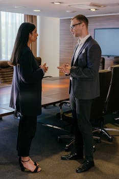 Two professionals engaged in discussion inside a modern conference room setting.